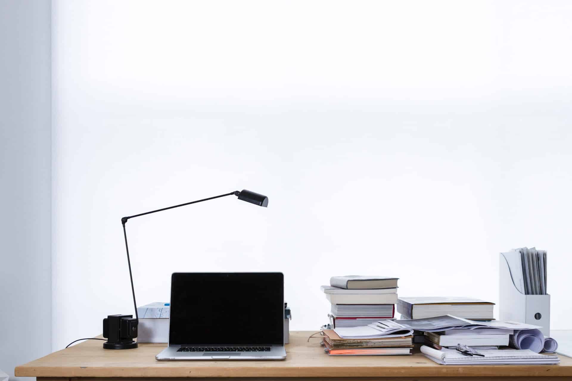 documents & laptop on a desk against a white wall